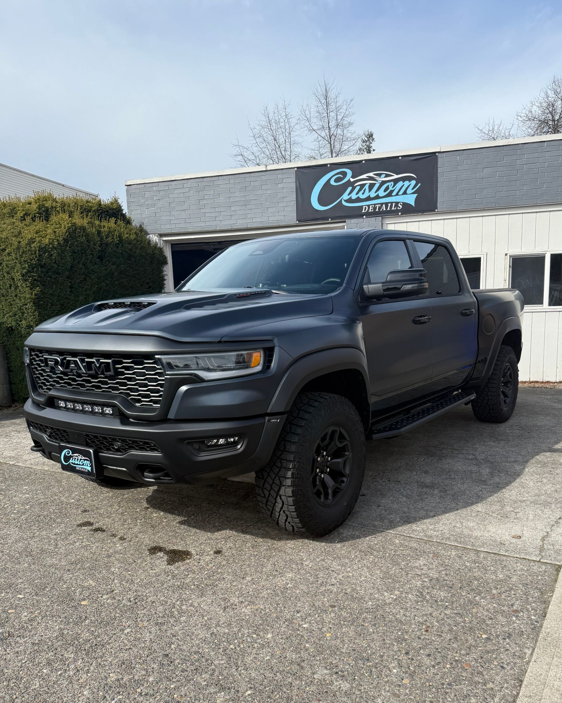 Black lifted pickup truck parked outside a building with a blue sign on a gravel lot