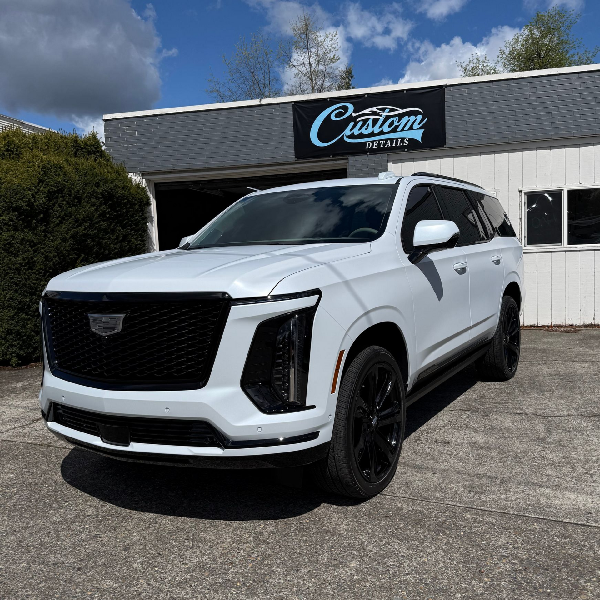 White Cadillac SUV parked outside a custom shop on a sunny day