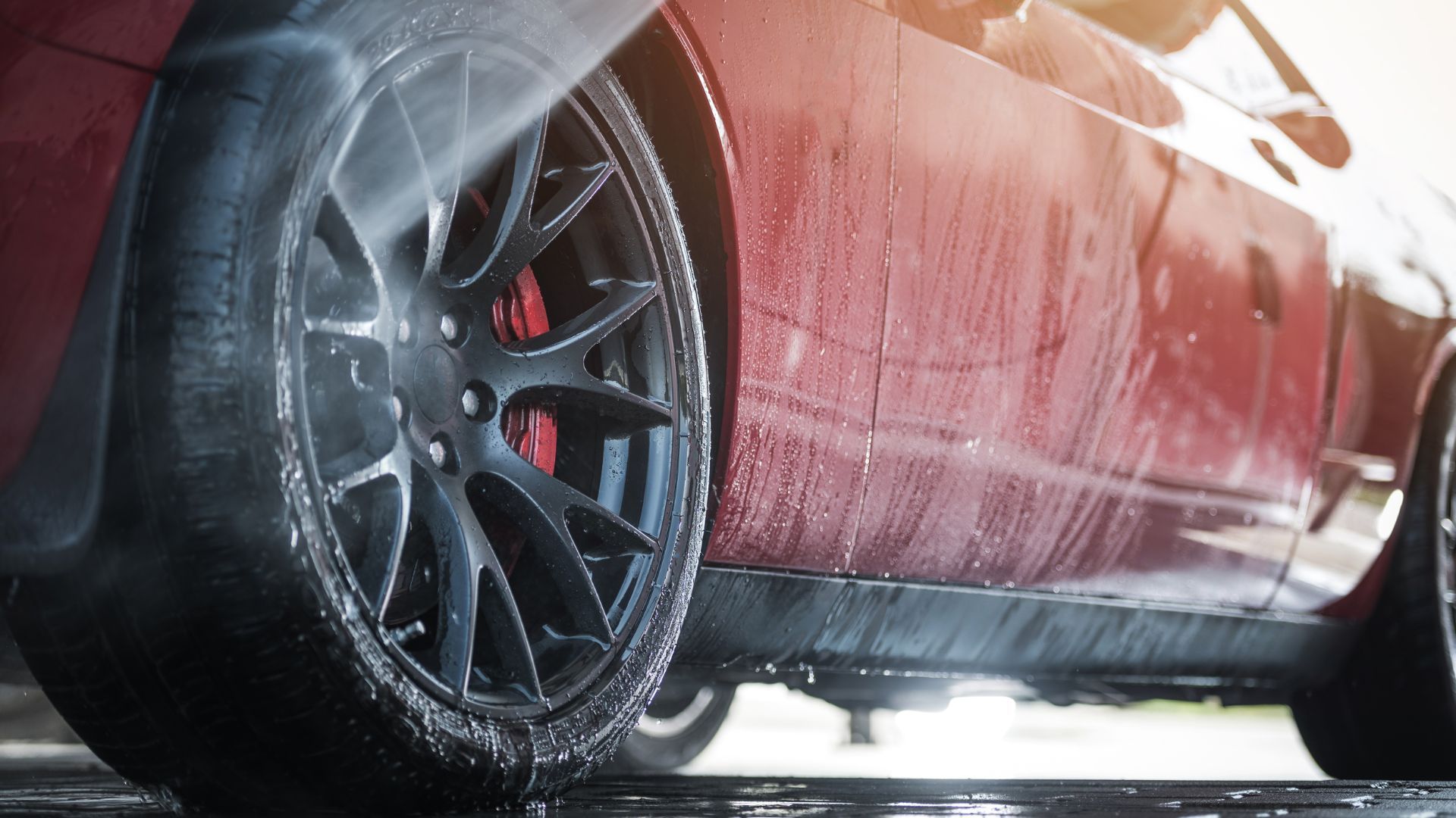 Water rinsing the black wheel and fender of a dark red car during an exterior wash.