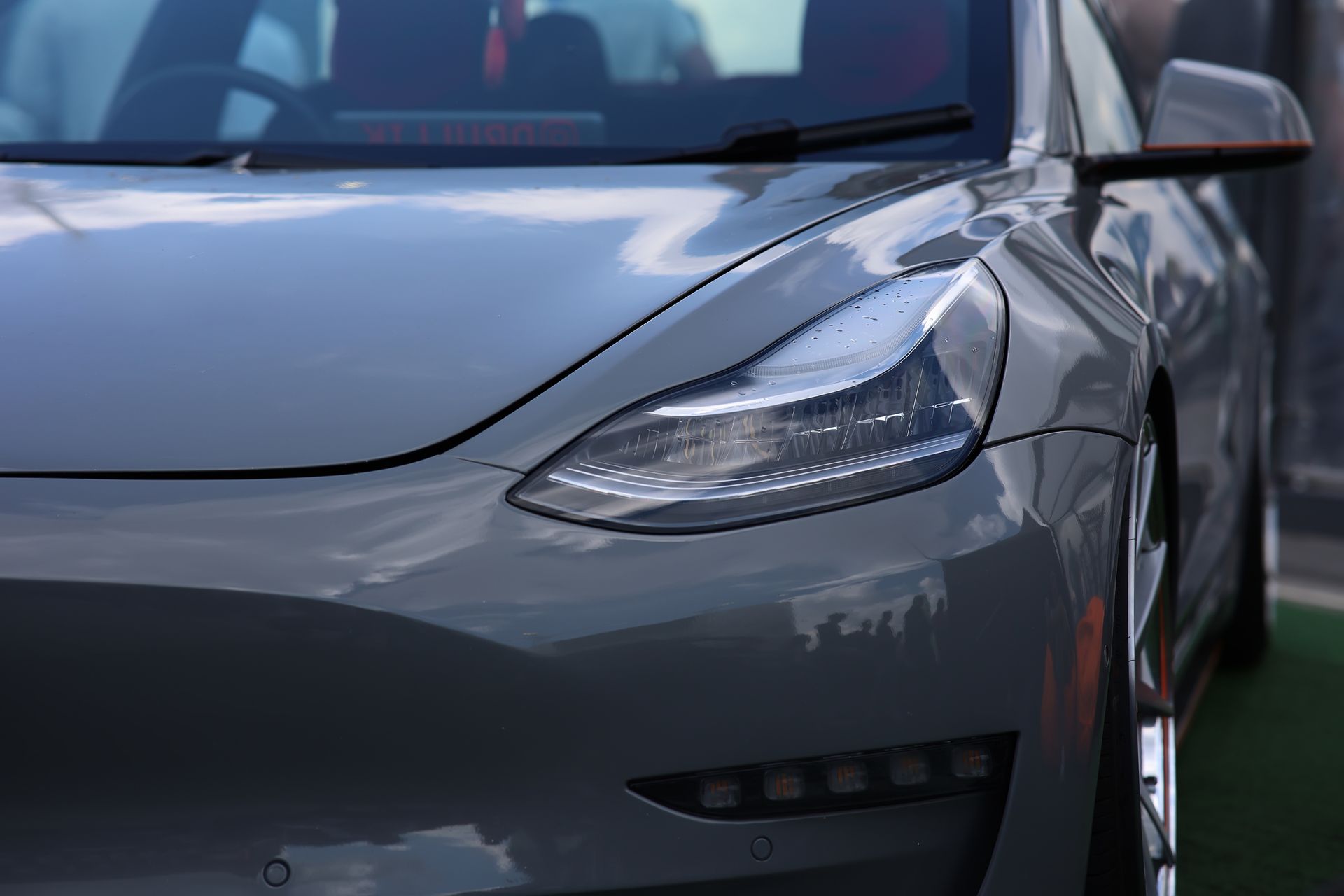 Close-up of a gray Tesla Model 3 front end, highlighting the headlight and sleek body design.